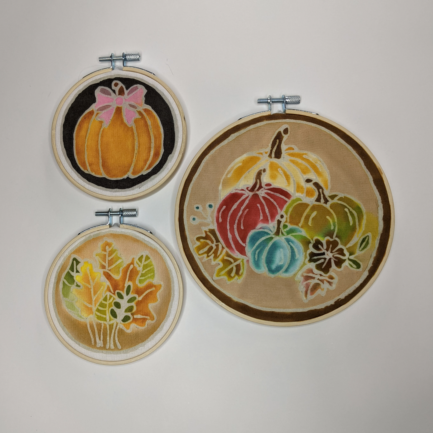 Three hoops with colored waxed designs of pumpkins and fall leaves.