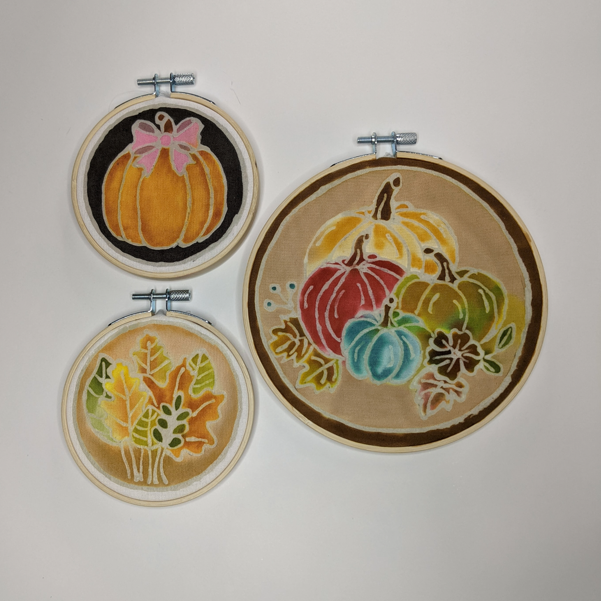 Three hoops with colored waxed designs of pumpkins and fall leaves.