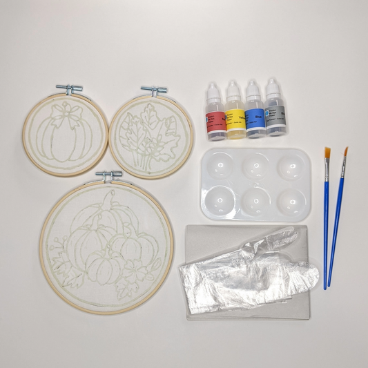 Hoops with pre-waxed design displayed alongside bottles of fabric dyes, palette, brushes, gloves and newsprint paper.