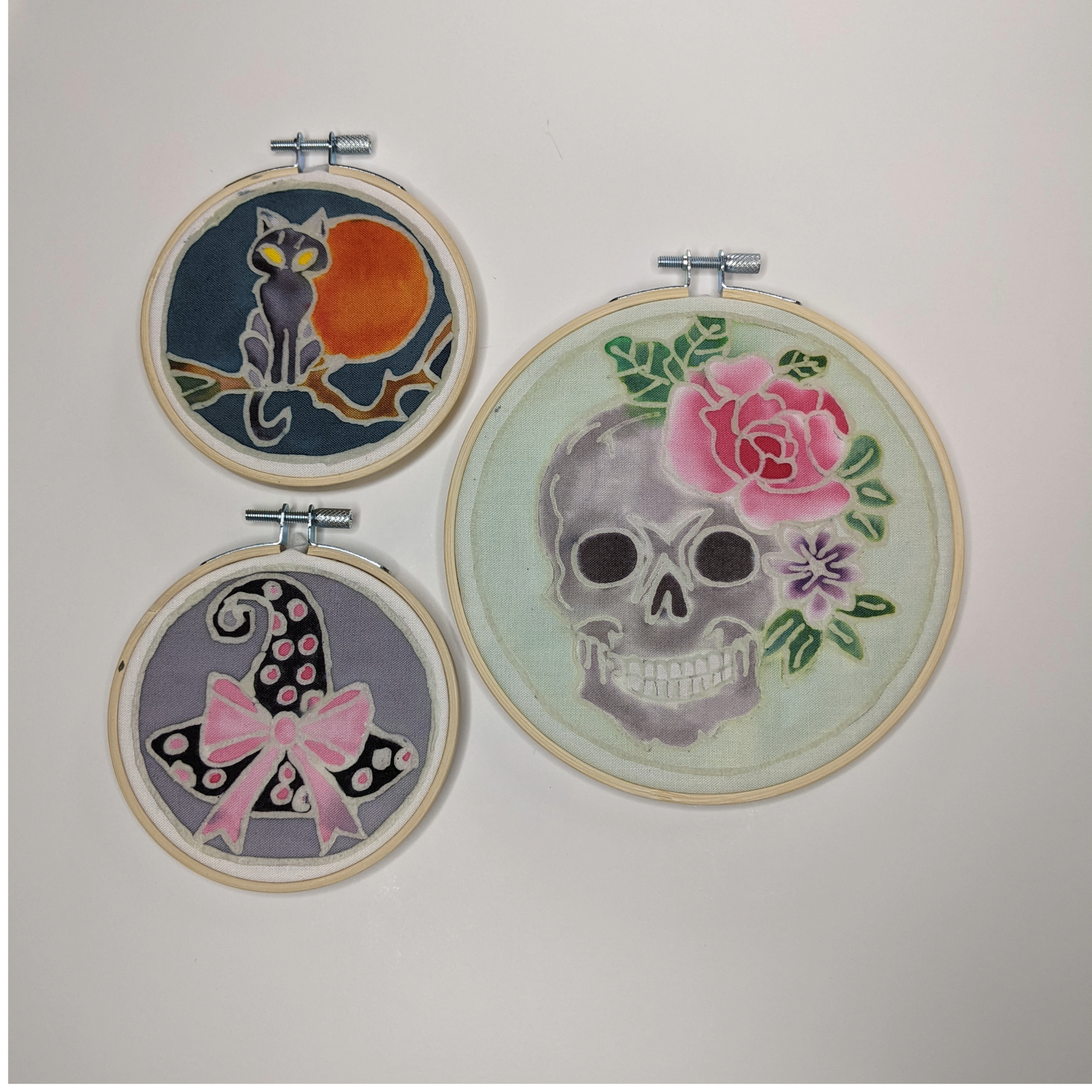 Three hoops with painted batik designs of skull, moonlit at and witch's hat with a bow.